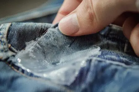A close-up of a hand using acetone to remove a hard spot of super glue from clothing, showing a clever hack