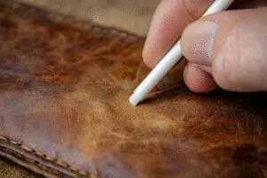 A hand carefully uses a Q-tip to remove a permanent marker stain from a leather surface, showing a leather rescue.