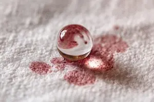 A fast solutions guide for how to get blood stains out of sheets, showing hydrogen peroxide cleaning a spot on white fabric