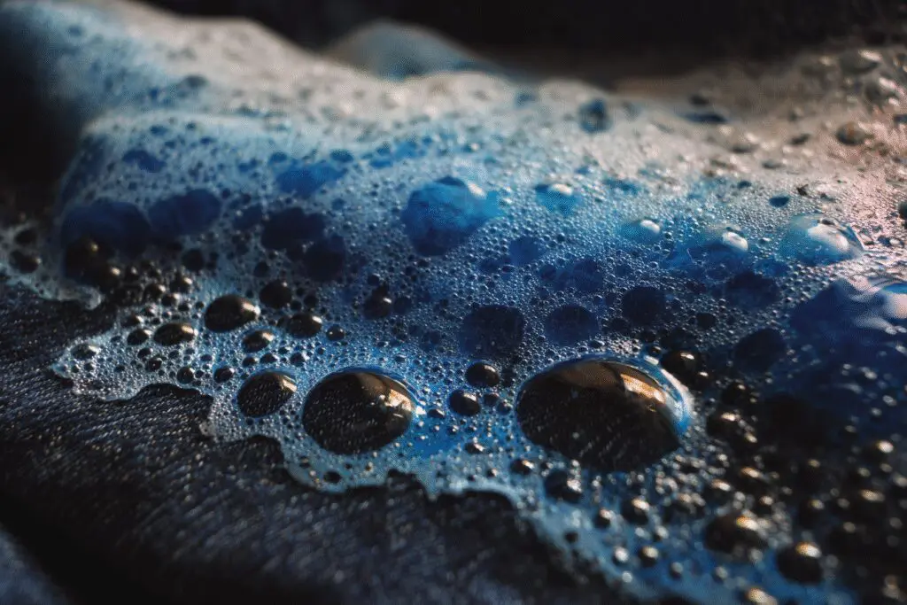 A pre-treatment method for the FAQ on how to get motor oil out of clothes, showing dish soap being used on a greasy stain