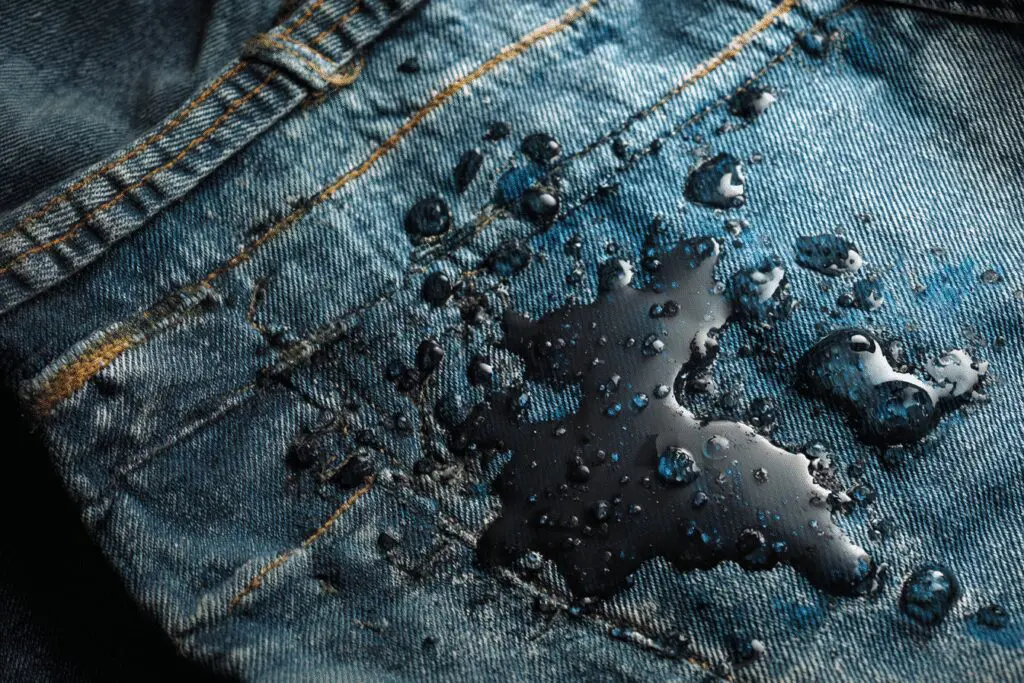 One of 5 methods for how to get motor oil out of clothes, showing dish soap being used to pre-treat a greasy stain on jeans.