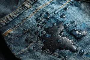 One of 5 methods for how to get motor oil out of clothes, showing dish soap being used to pre-treat a greasy stain on jeans.