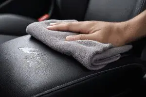 A fast fix for how to get sunscreen out of leather seats, showing a hand wiping the stain away with a microfiber cloth