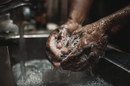 The ultimate guide on how to get gasoline smell out of hands fast, showing a pair of hands being washed with a strong cleaning soap
